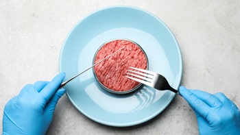 Mani con guanti in lattice che impugnano posate davanti a piatto con carne trita